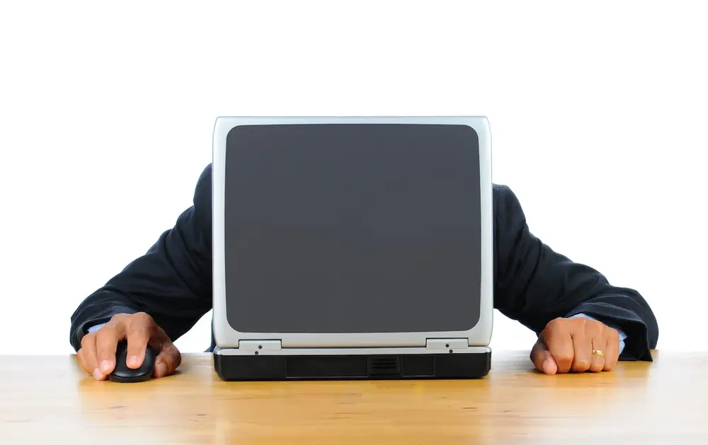 Businessman assis derrière un ancien ordinateur gris rectangulaire sur un bureau en bois, moment neutre illustrant la frustration liée à la technologie